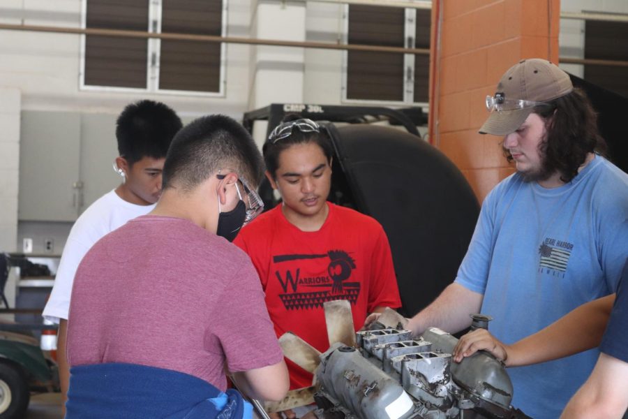 Four students stand around a car engine to study its functions.